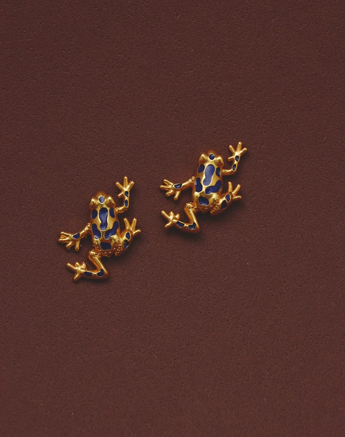 Gold plated blue enamel frog stud earrings on burgundy background