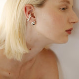 Close-up of a woman wearing silver earrings with a plain background.