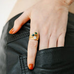Hand wearing gold rings with gemstones on a plain background. 