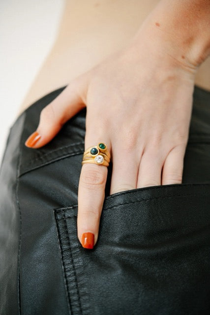 Hand wearing gold rings with gemstones on a plain background. 