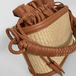 Brown leather and straw handbag on a light gray background.