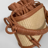 Brown leather and straw handbag on a light gray background.