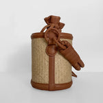 Small woven basket with brown leather straps and knot on a white background.