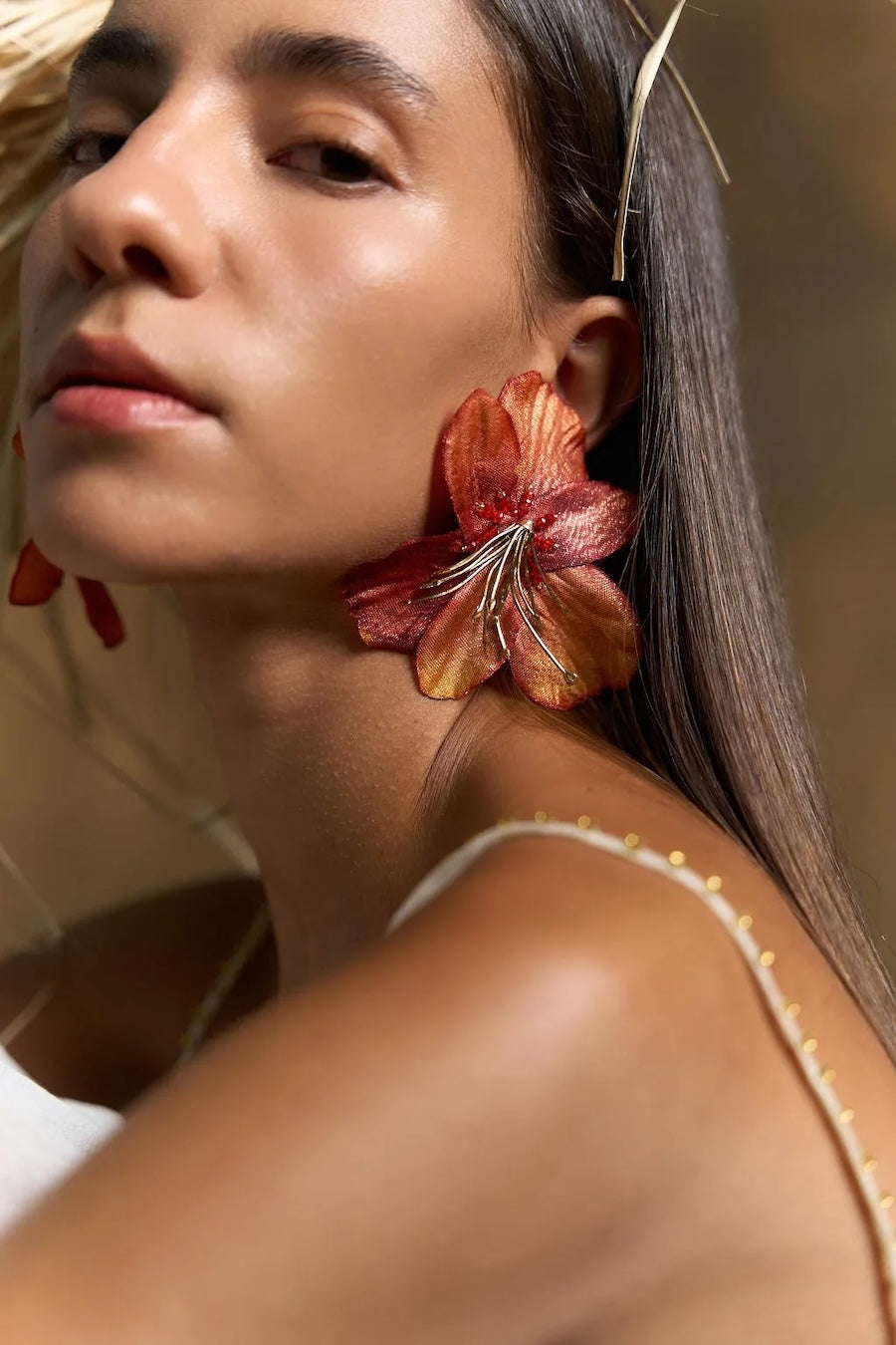 Woman wearing large orange floral earrings with a neutral background