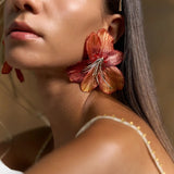 Woman wearing large orange floral earrings with a neutral background