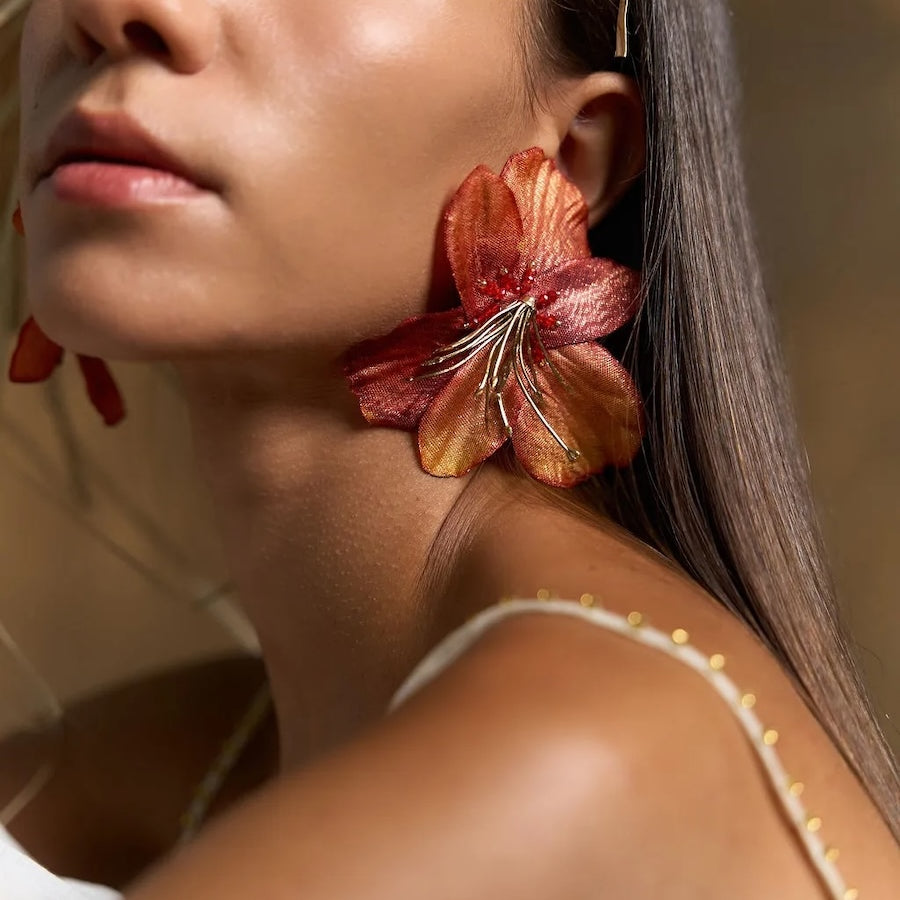 Woman wearing large orange floral earrings with a neutral background