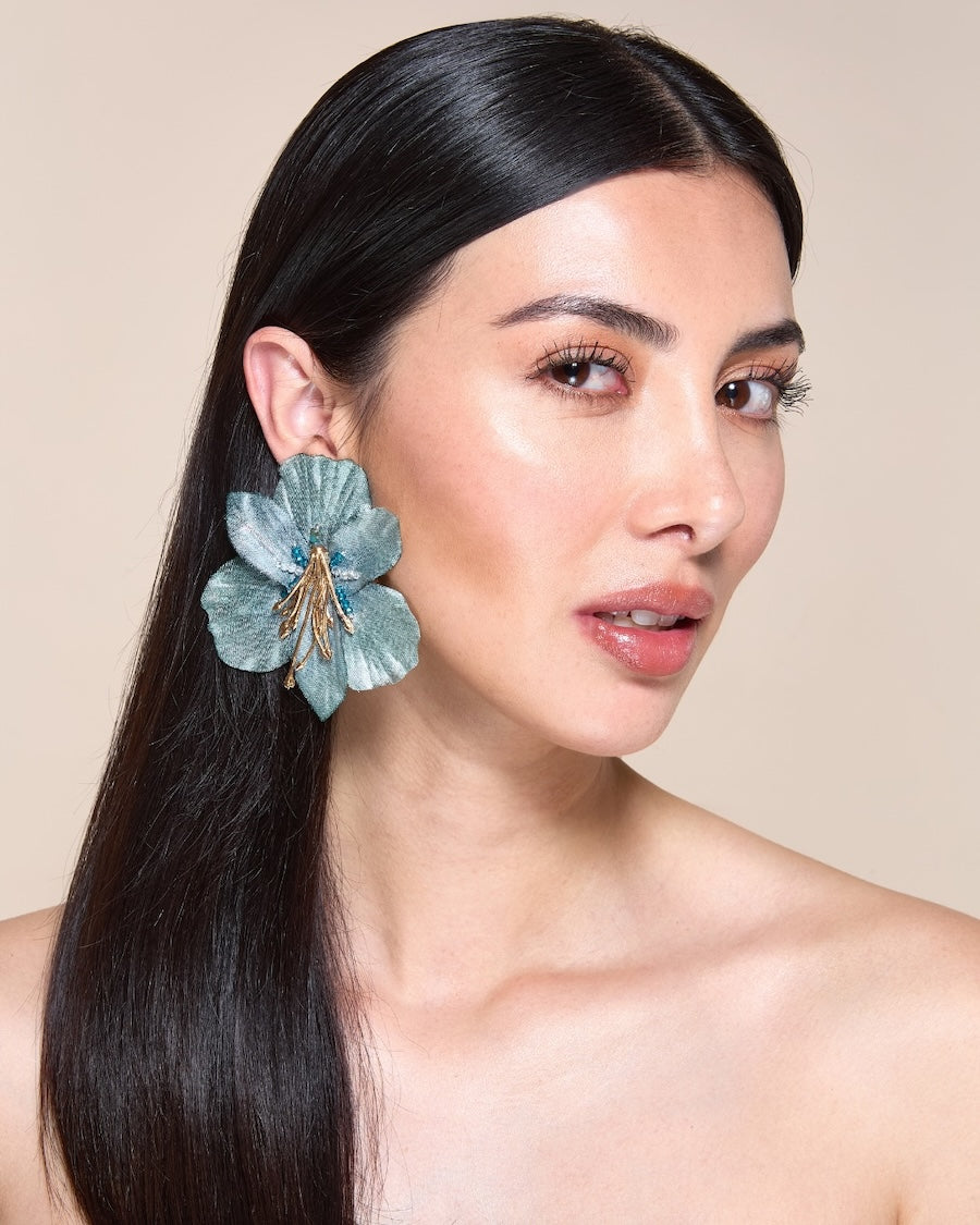 Woman wearing a large blue floral earring against a beige background
