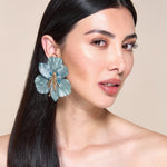 Woman wearing a large blue floral earring against a beige background