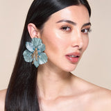Woman wearing a large blue floral earring against a beige background