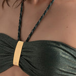 Closeup of a green bikini halter top with gold clasp on a person against a neutral background.
