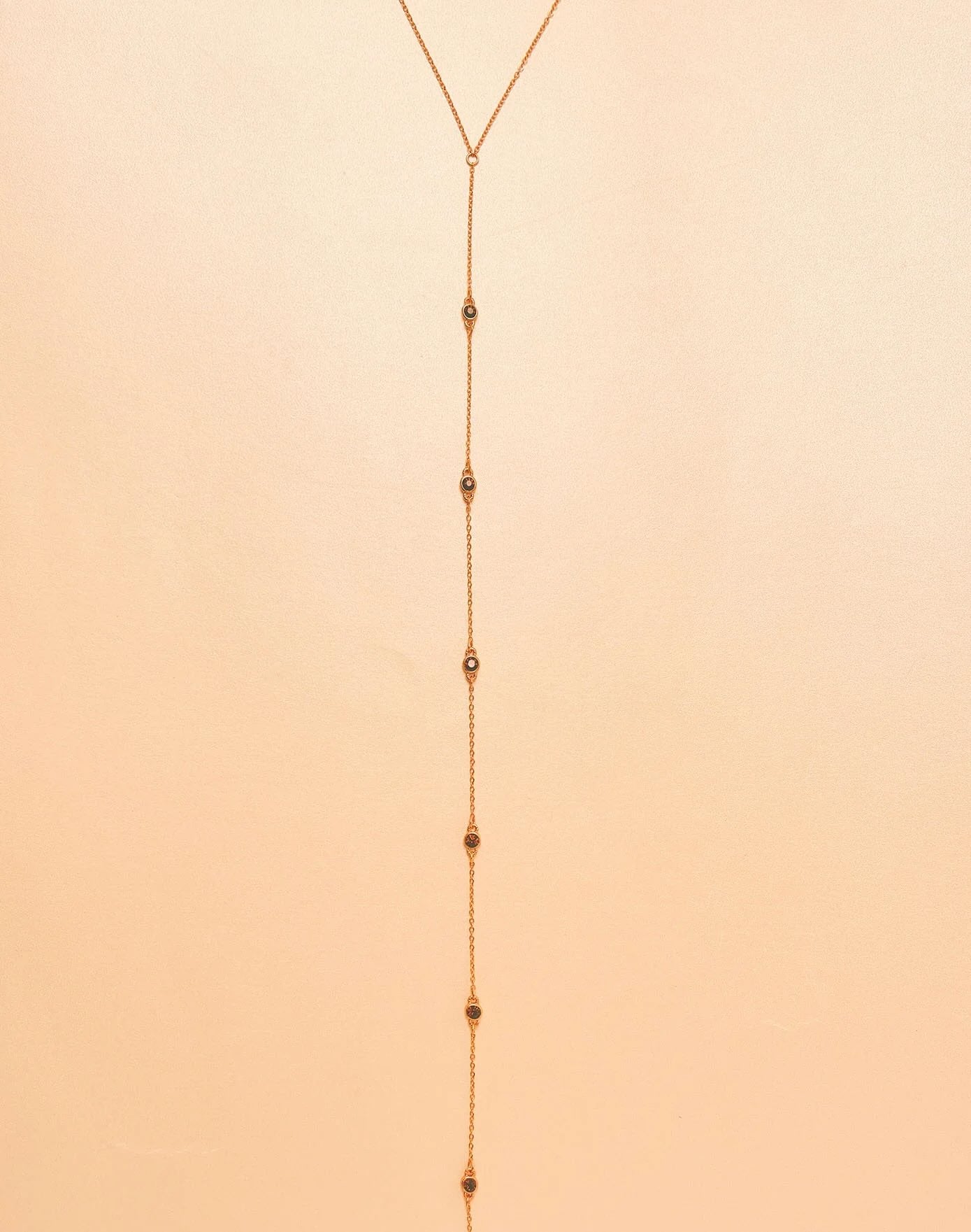 Gold plated lariat necklace on a beige background