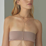 Woman wearing a beige strapless top with a gold necklace against a neutral background