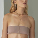 Woman wearing a beige strapless top with a gold necklace against a neutral background