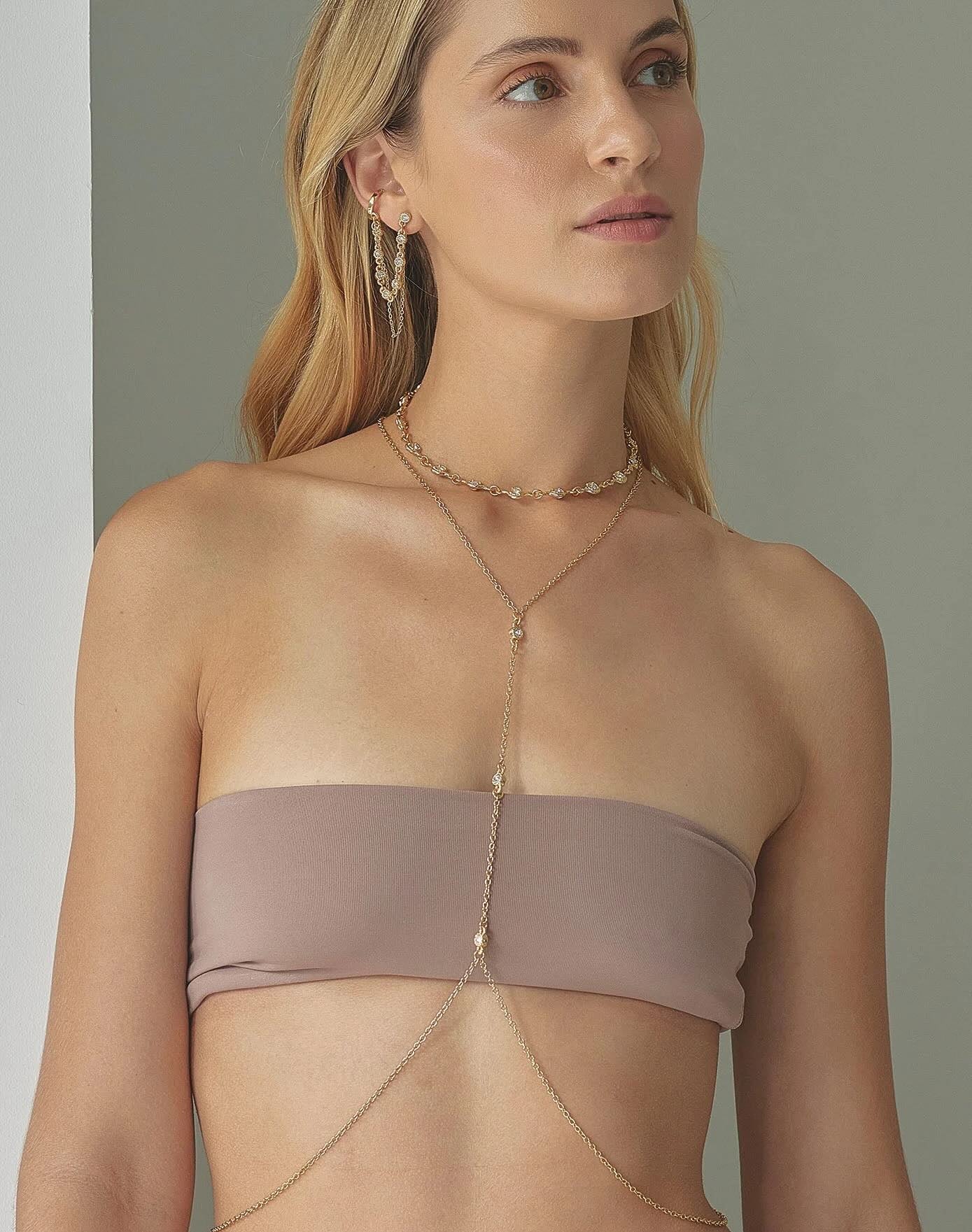 Woman wearing a beige strapless top with a gold necklace against a neutral background