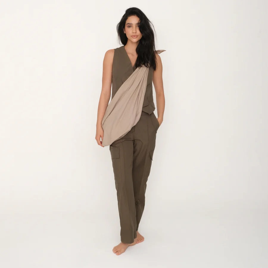 Woman wearing an olive green top and brown pants with a slouchy beige tote bag on a white background.