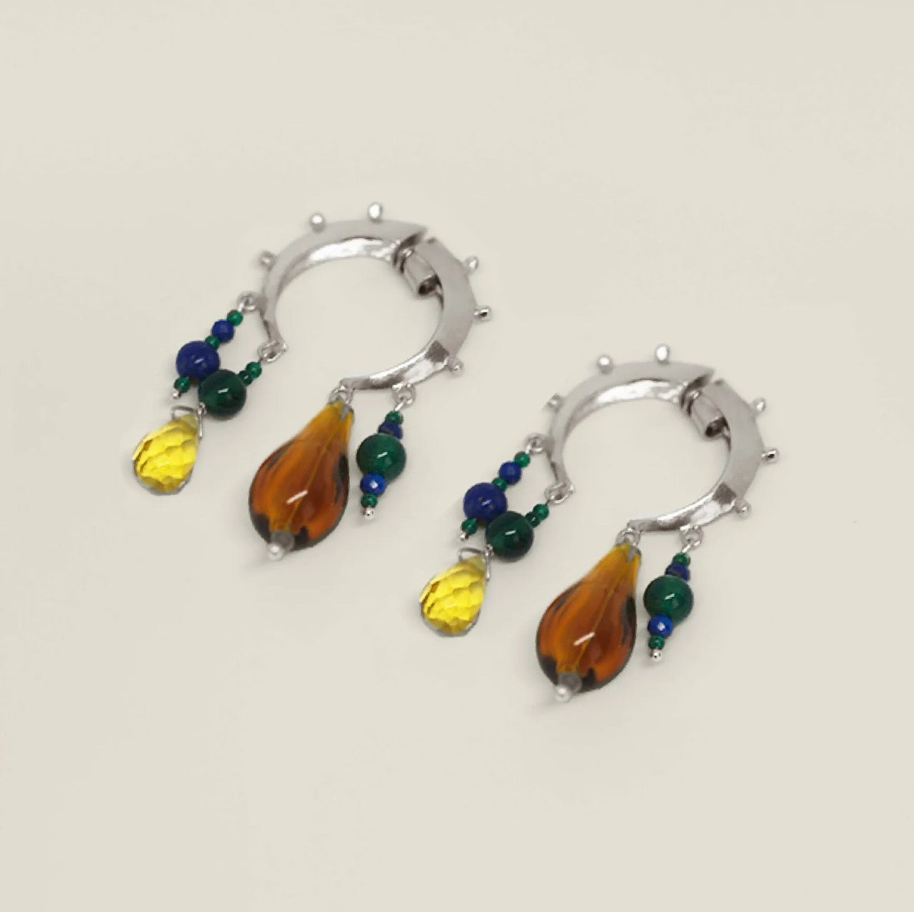 Pair of silver crescent hoop earrings with colorful teardrop-shaped beads on a white background.