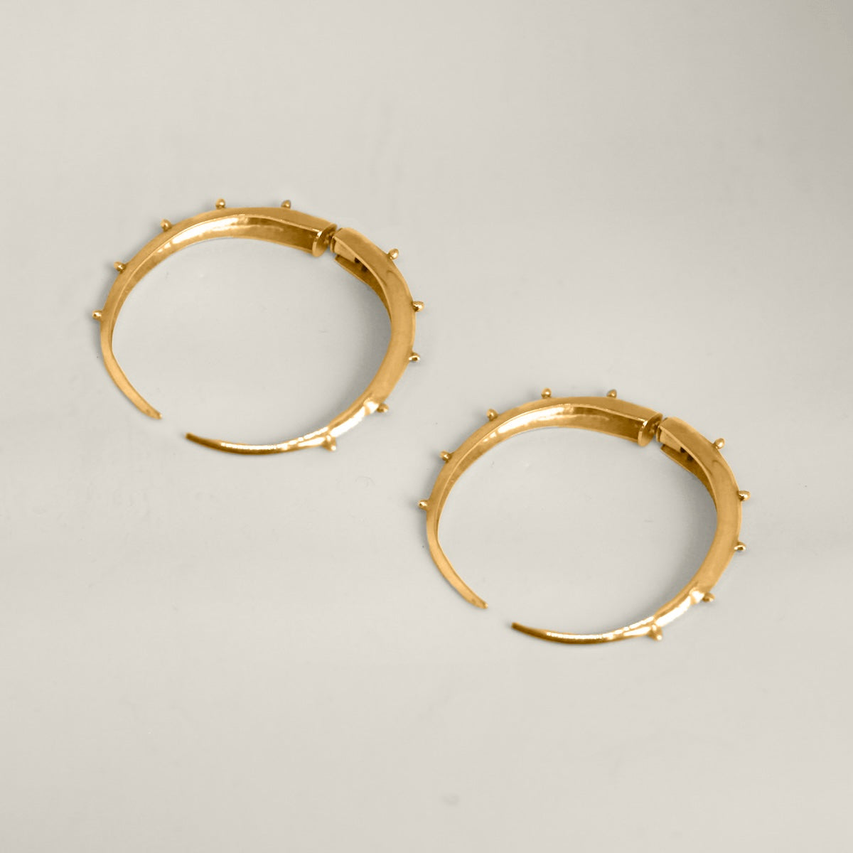 Gold hoop earrings with small spikes on a light gray background.