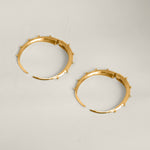 Gold hoop earrings with small spikes on a light gray background.