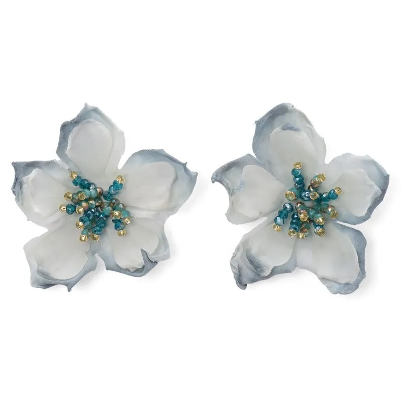 Pair of floral earrings with white and blue petals and gold centers on a white background