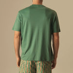 Man wearing a green t-shirt and fish patterned swim shorts on a beige background.