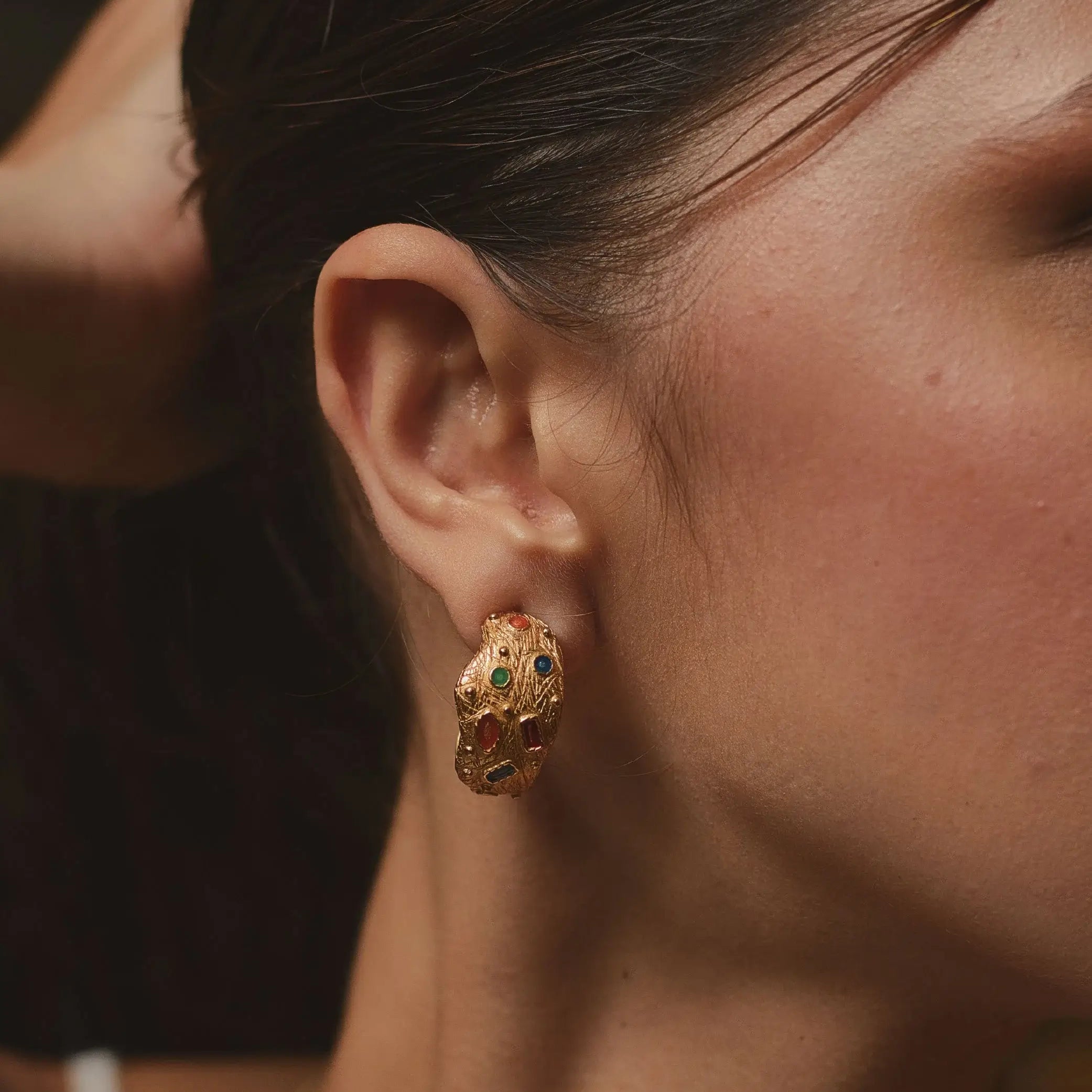 Close-up of a person wearing gold earrings with green gemstones.
