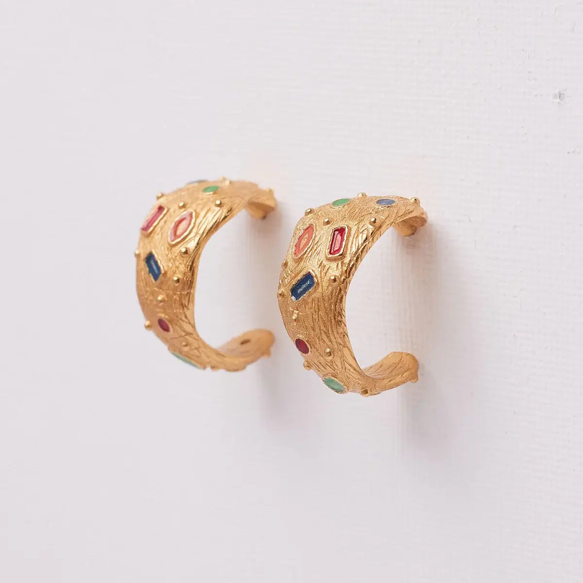 Gold hoop earrings with colorful gemstones on a white background.