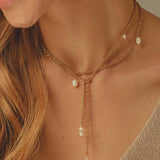 Close-up of a woman wearing a gold necklace with pearl drops.