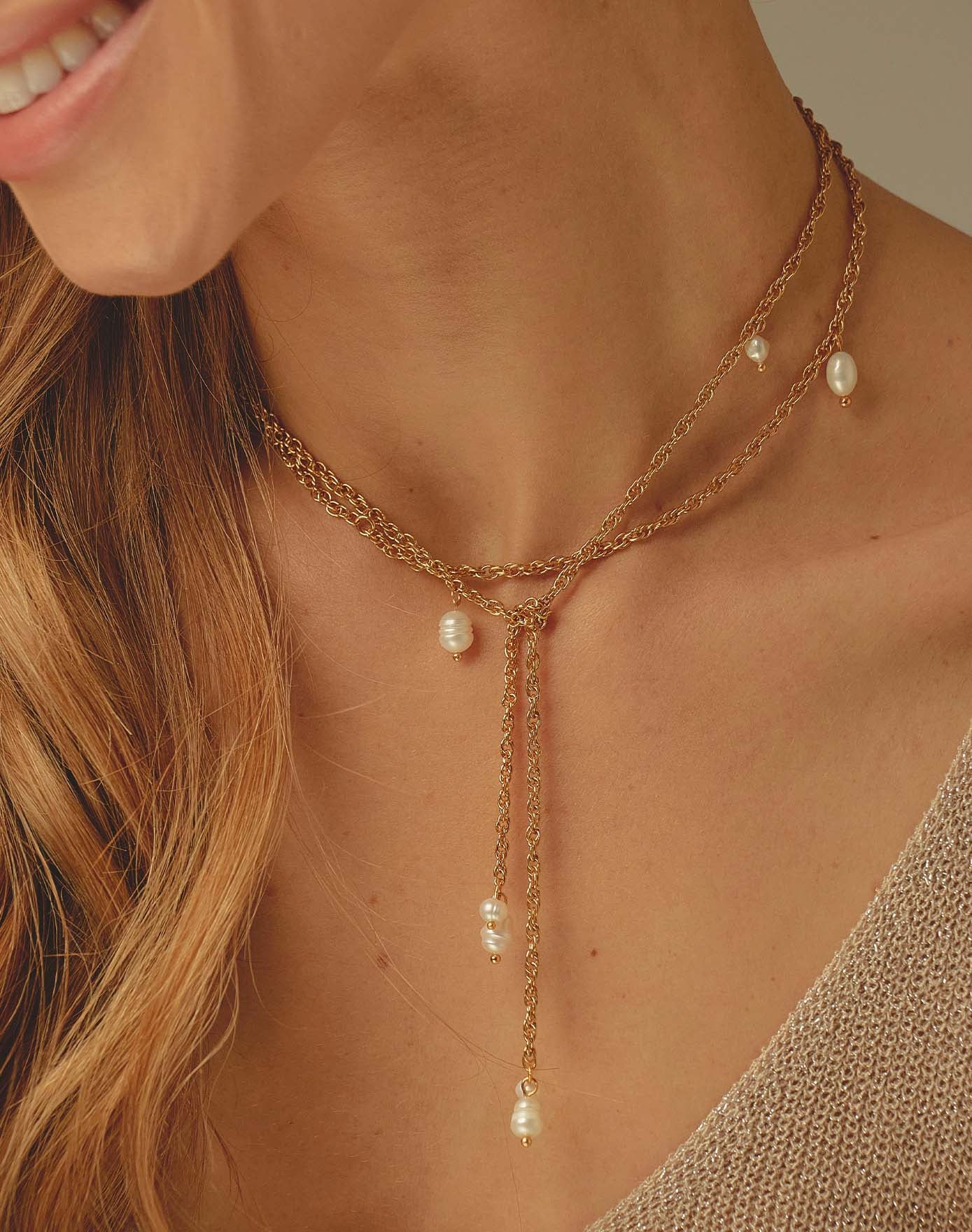 Close-up of a woman wearing a gold necklace with pearl drops.