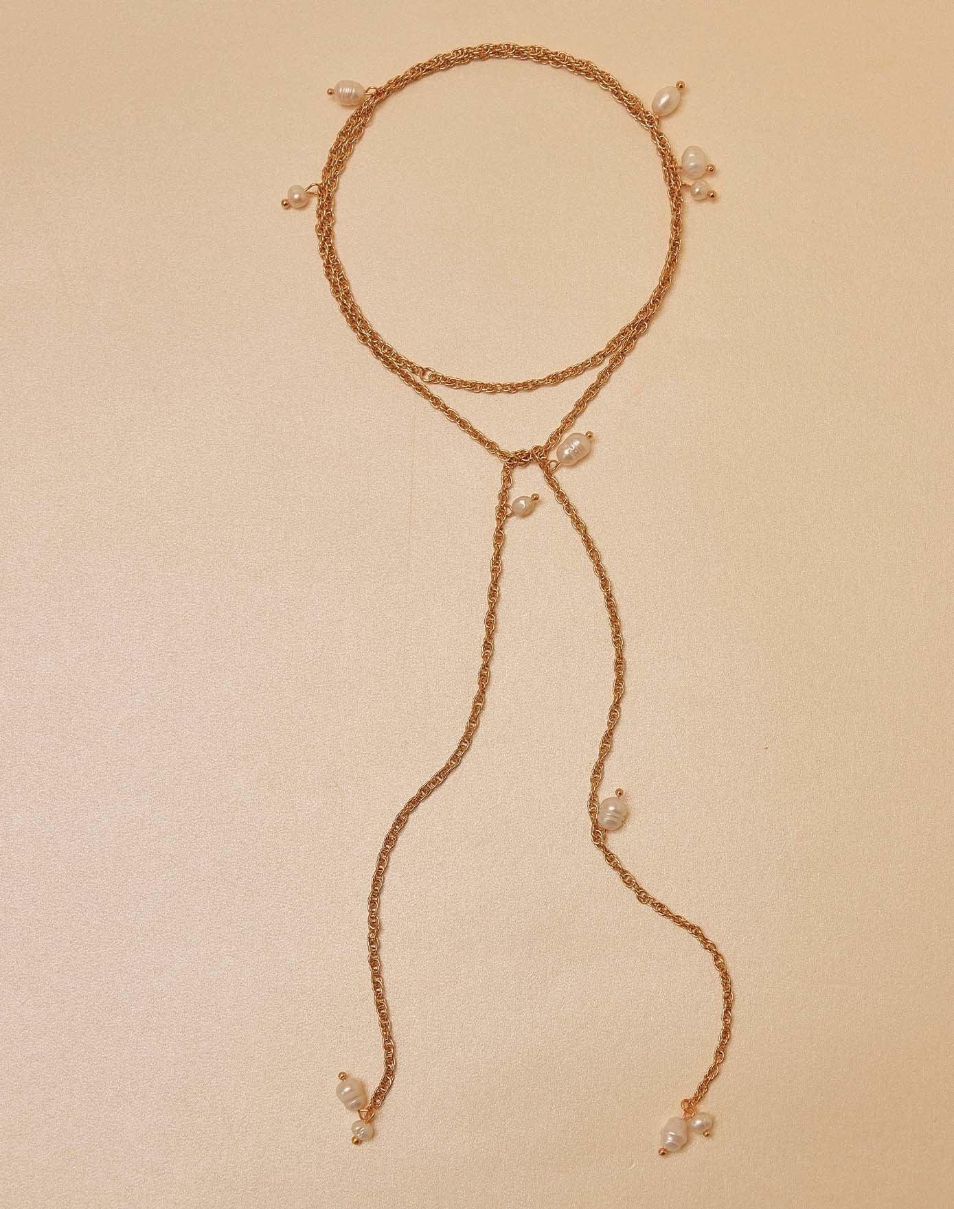 Delicate gold necklace with small pearls on a beige background
