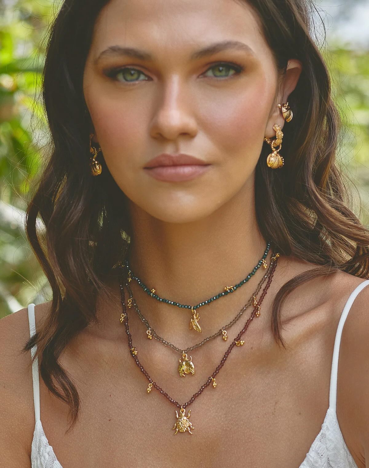 Woman wearing layered necklaces and earrings with a natural background