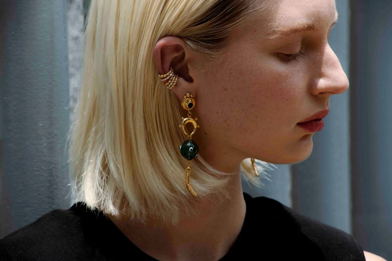 Close-up of a person wearing gold statement earrings with gold/silver cuffs in a blurred background.