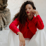 Woman in a red blouse and white pants sitting against a stone wall.