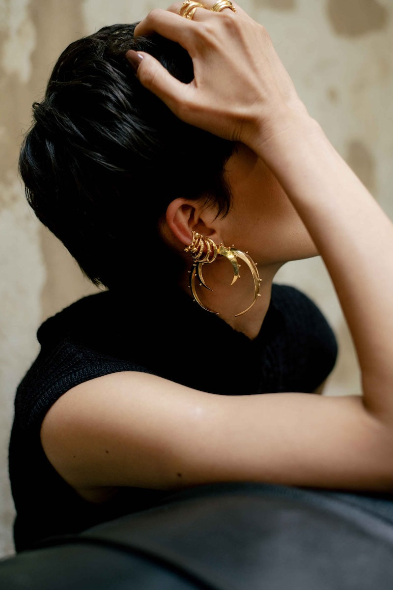 Person wearing gold hoop earrings with a neutral background.
