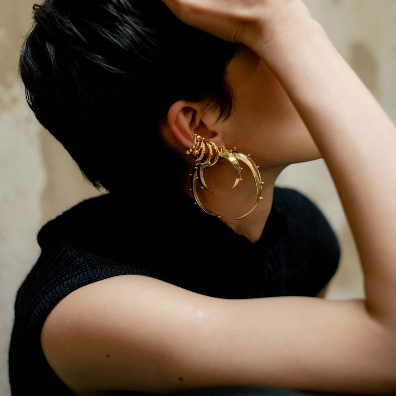 Person wearing gold hoop earrings with a neutral background.