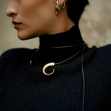 Person wearing gold hoop earrings and a black turtleneck with a swirl statement necklace.