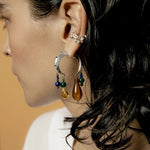 Close-up of a person wearing a crescent earring with dangling beads against a neutral background.