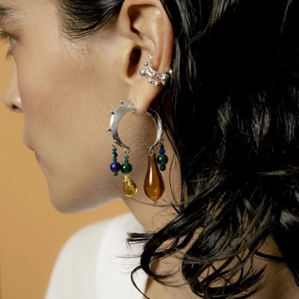 Close-up of a person wearing a crescent earring with dangling beads against a neutral background.