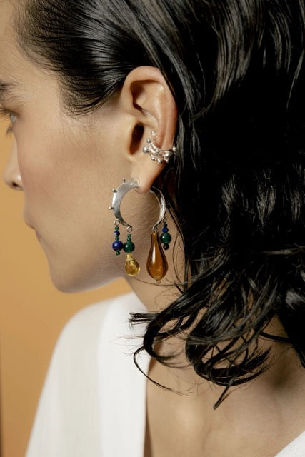 Close-up of a person wearing a crescent earring with dangling beads against a neutral background.