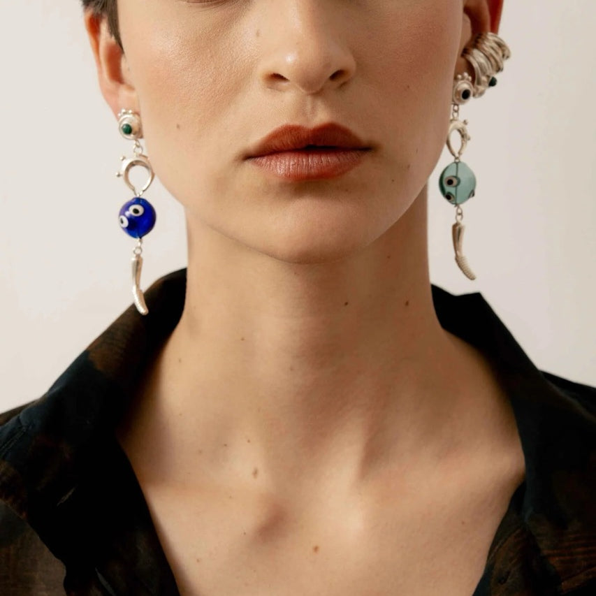 Close-up of a person wearing silver earrings with dark and light blue accents in front of neutral background.