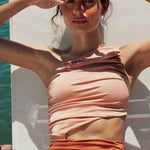 A woman wearing an orange one-piece swimsuit with elegant one-shoulder silhouette and a triangular side cutout for a modern, sculptural look.