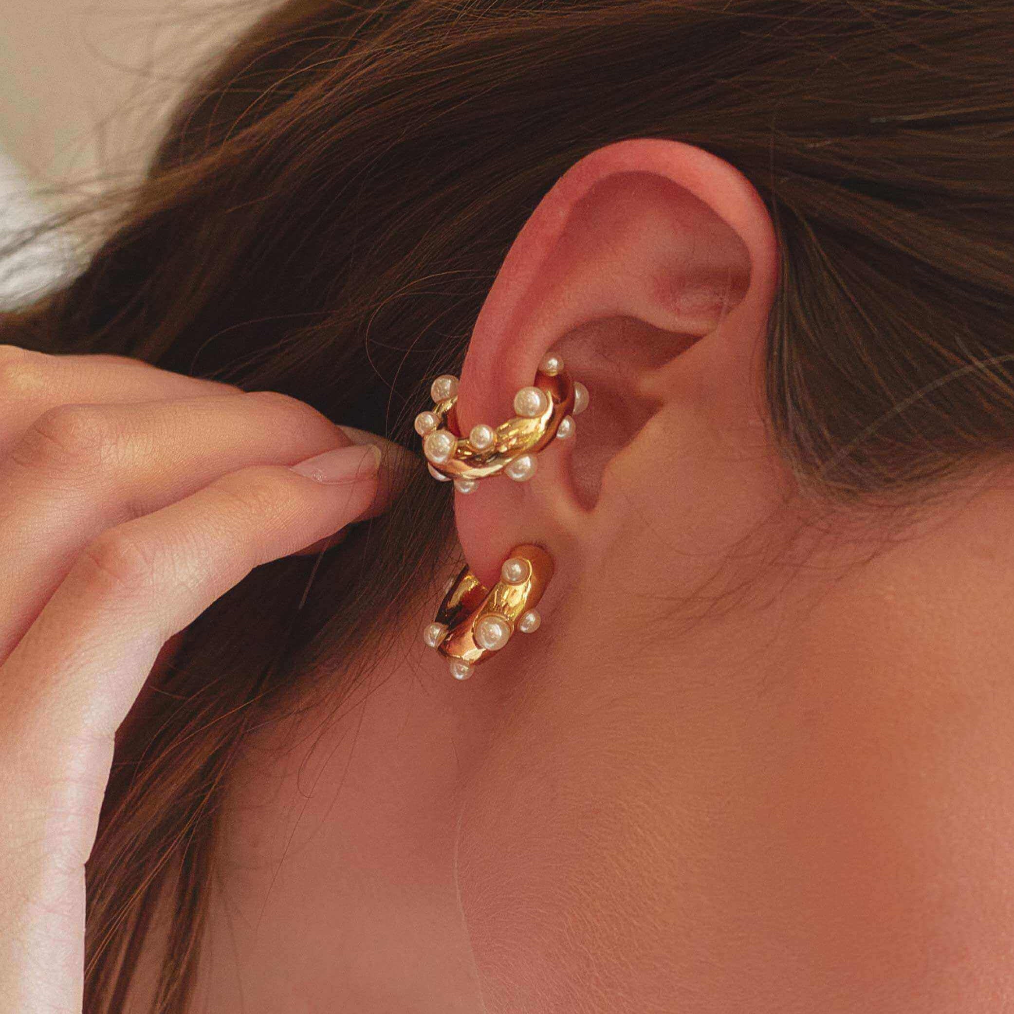 Close-up of gold and pearl earring ear-cuff set worn on an ear with a blurred background.