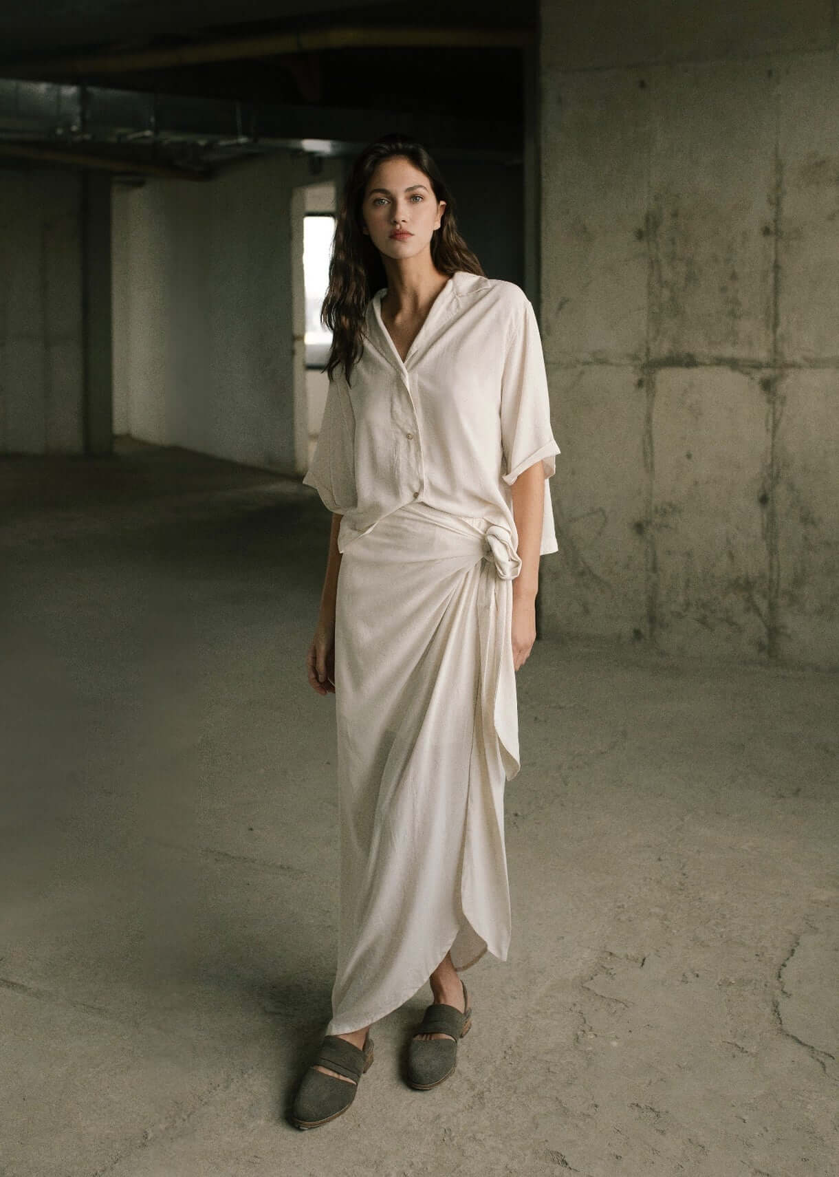 Woman wearing a white top and white skirt outfit in an industrial setting.