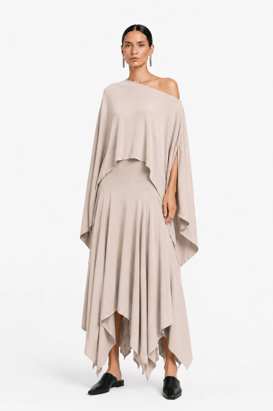 Woman wearing a beige one-shoulder blouse and layered skirt on a white background.
