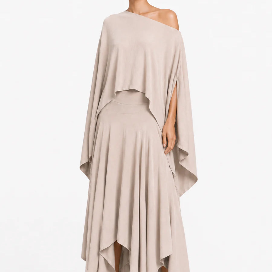 Woman wearing a beige one-shoulder blouse and layered skirt on a white background.