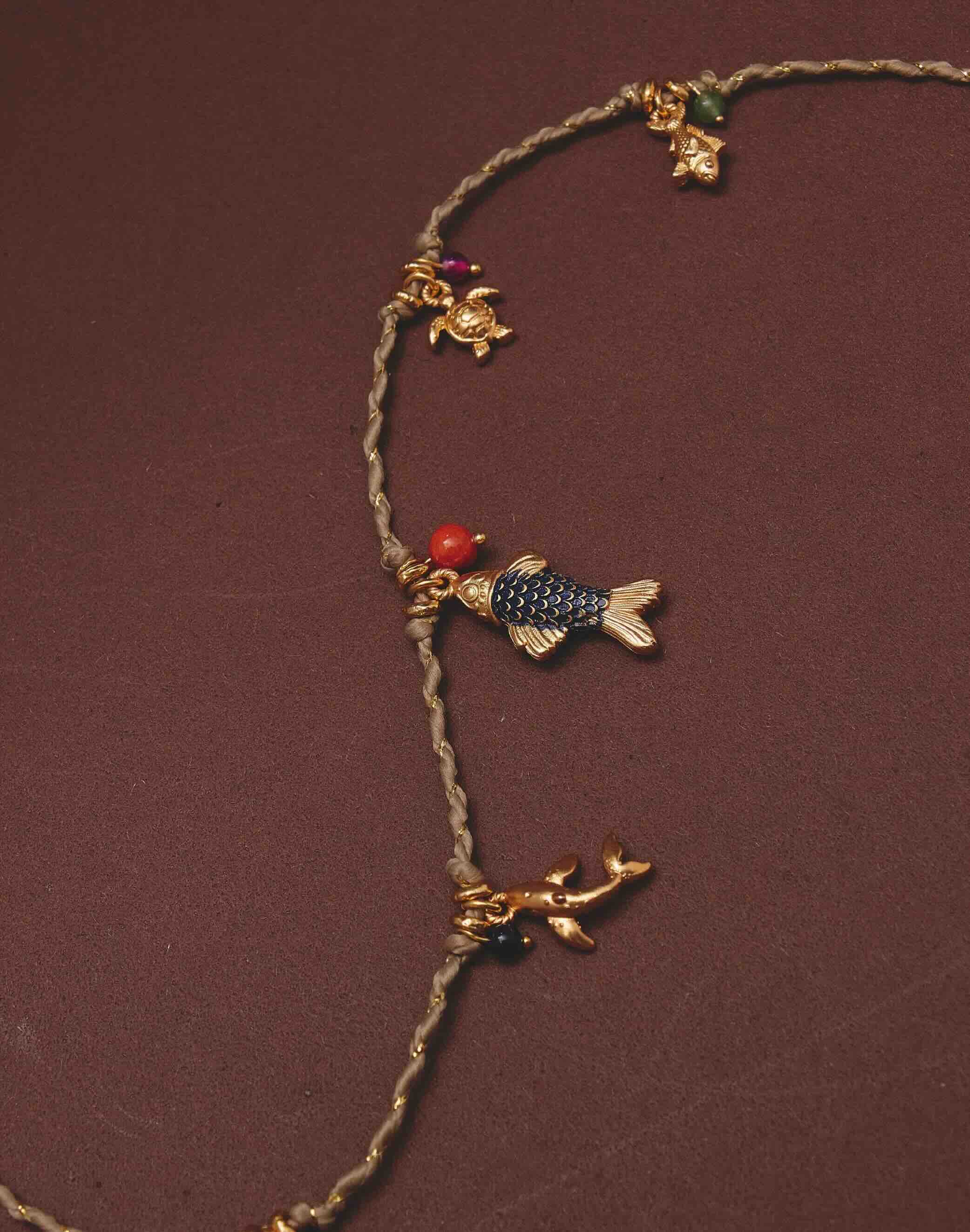 Necklace with fish and turtle charms on a brown background