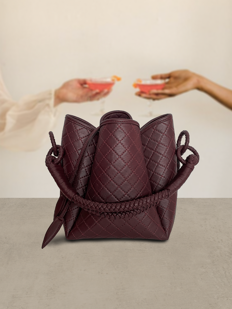 burgundy leather handbag with two hands holding drinks behind it.