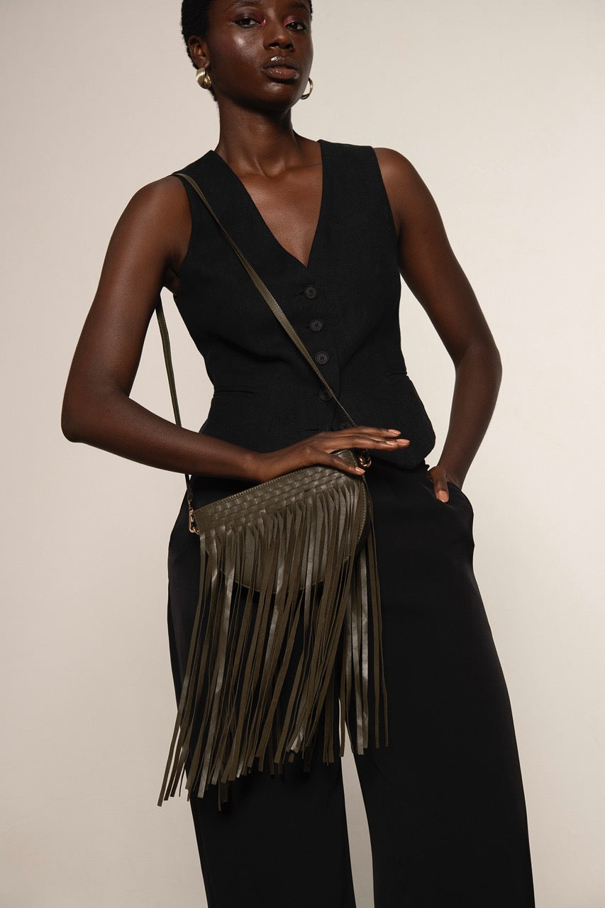 Woman holding a green fringe handbag against a plain background.