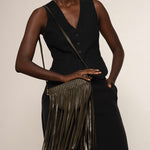 Woman holding a green fringe handbag against a plain background.