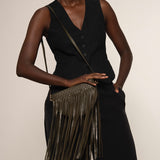 Woman holding a green fringe handbag against a plain background.