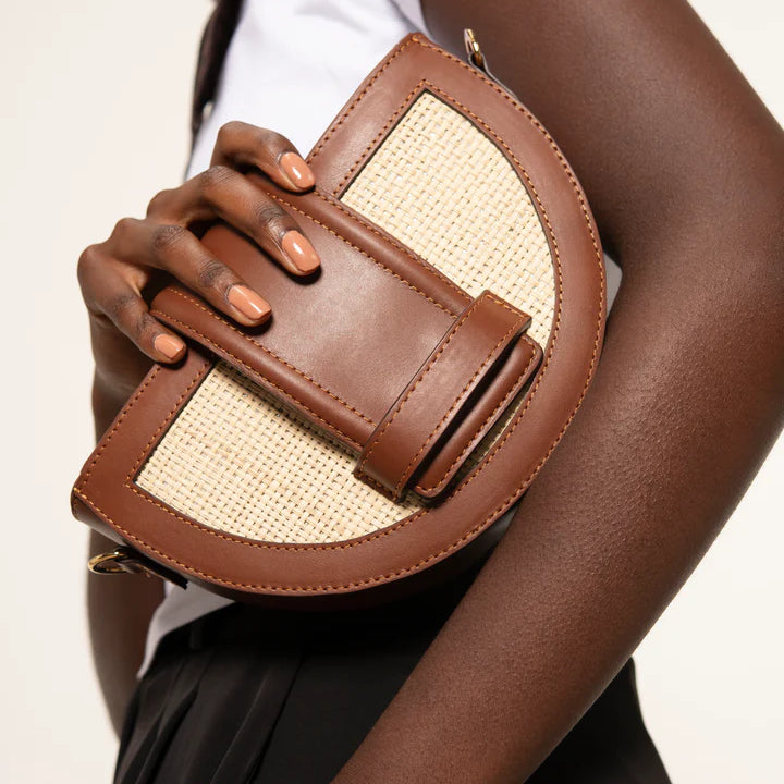 Person holding a brown leather handbag with beige accents against a plain background.